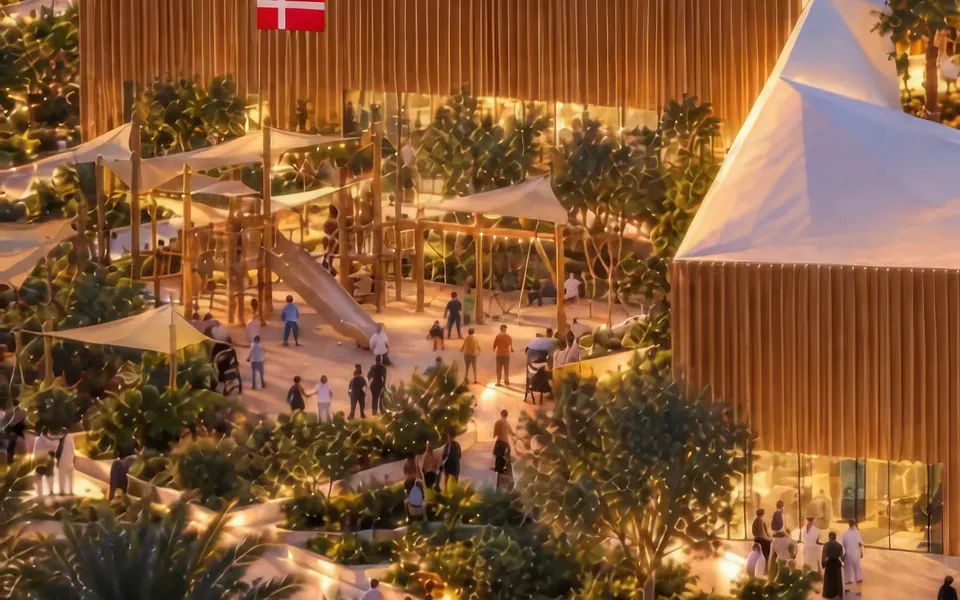 Landscaped grounds beside the pavilion at dusk: planted terraces, lit paths and shade sails, with visitors.